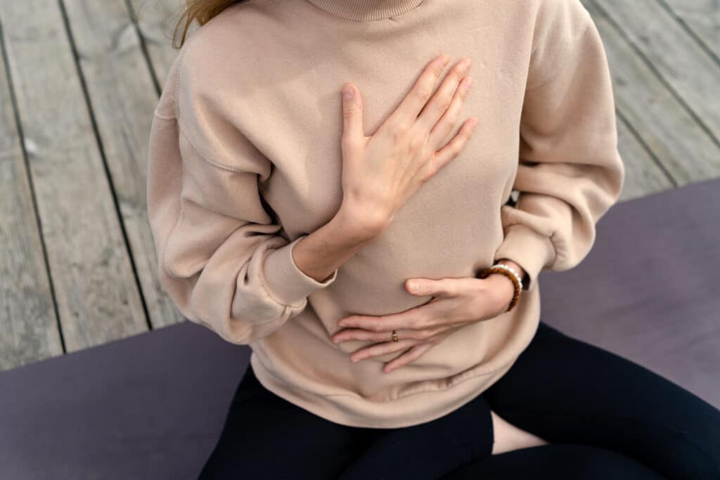 Méditation & Respiration : Calme et pleine conscience. Femme en pull, mains sur poitrine et ventre pour méditation ou respiration consciente sur tapis de yoga. Calme, sérénité.